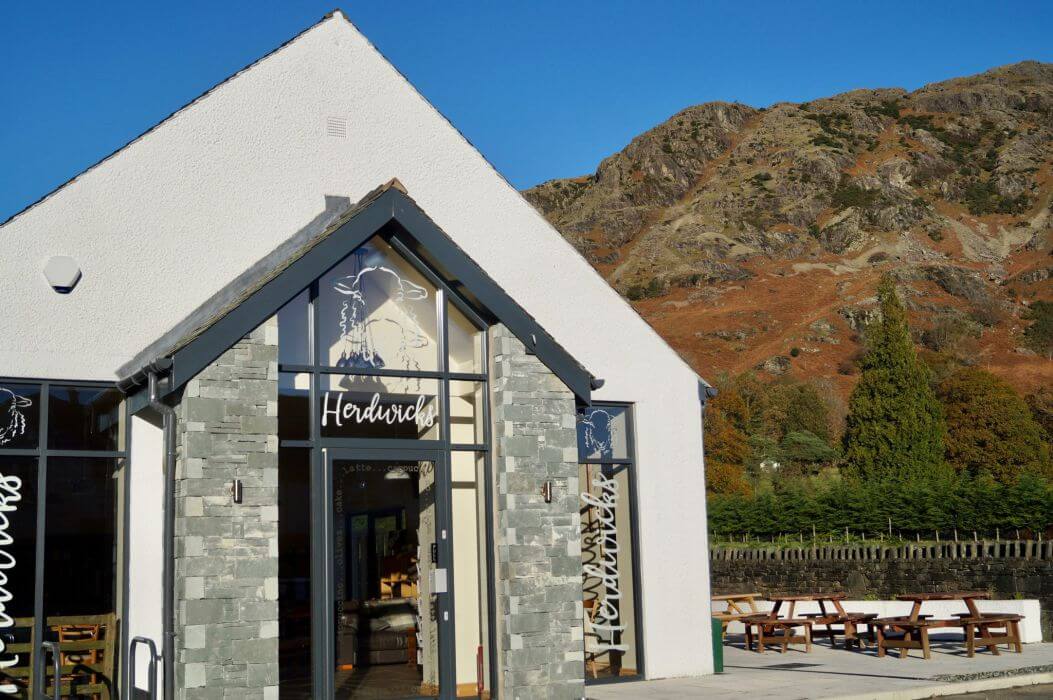 The front of Herdwicks café on Yewdale Road, with picnic benches outside and the fell behind