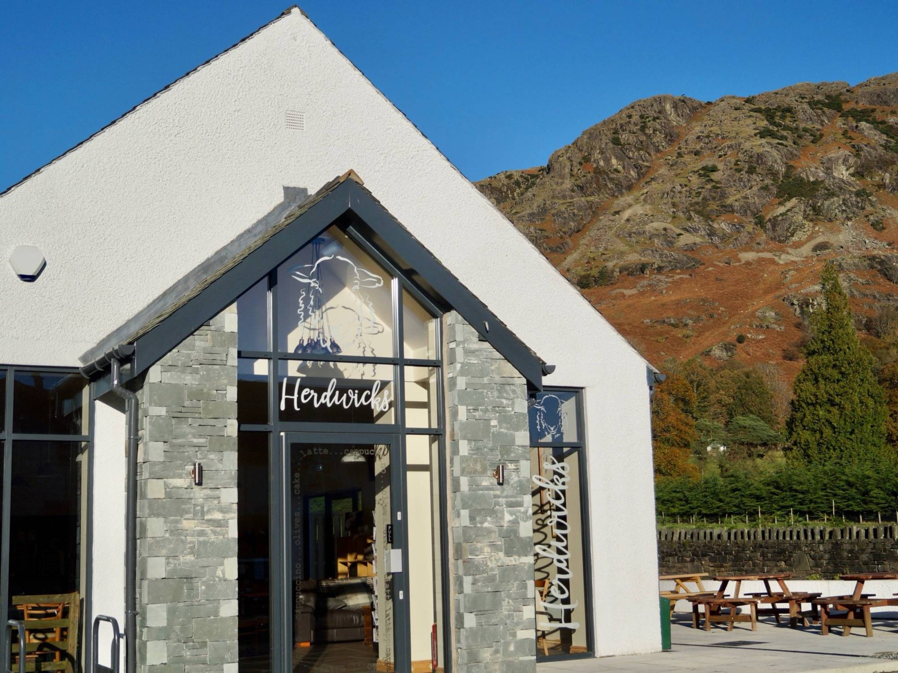Herdwicks café — a whitewashed gable with slate pillars, the Coniston fells rising behind it